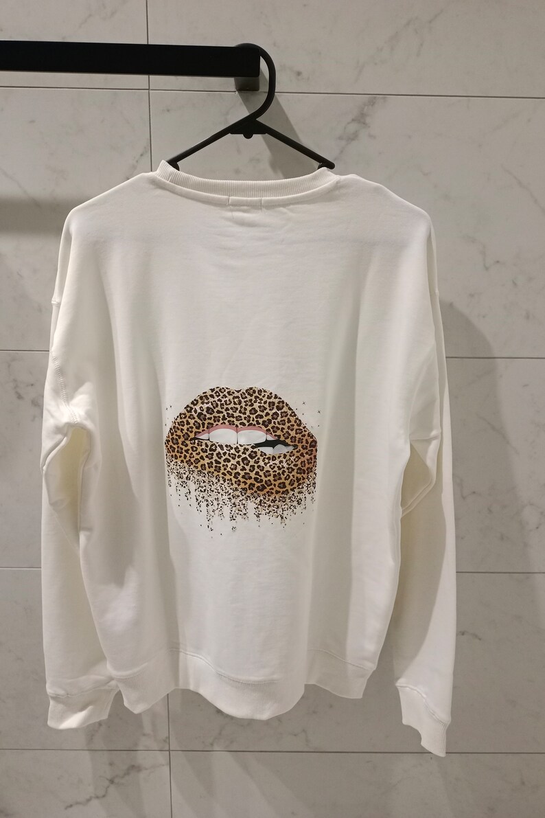 Pu&ograve; includere: Felpa bianca con un design di labbra a stampa leopardata sul retro.