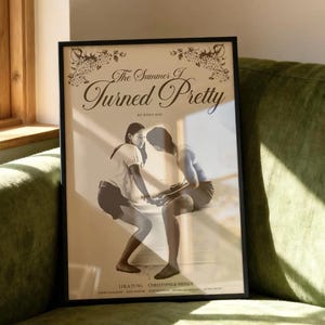 Puede incluir: Póster enmarcado con el título "The Summer I Turned Pretty" en escritura elegante. La imagen en sepia muestra dos figuras interactuando. El marco negro descansa contra un sofá verde, cerca de una ventana.