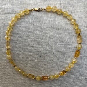 May include: A yellow citrine gemstone necklace with a gold clasp. The necklace is made of round and rectangular beads.