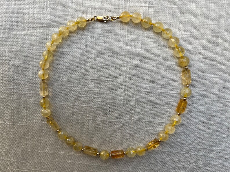 May include: A yellow citrine gemstone necklace with a gold clasp. The necklace is made of round and rectangular beads.