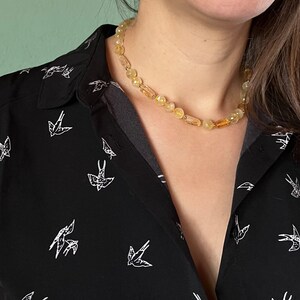 May include: A close-up of a woman wearing a black sleeveless shirt with a white bird pattern and a yellow amber necklace.