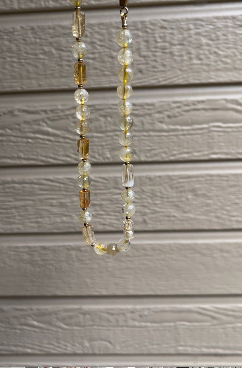 May include: A gold and clear crystal beaded necklace with a gold clasp. The necklace is made of round and rectangular beads.