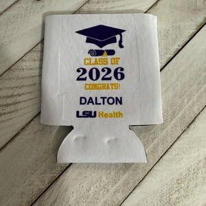 May include: White graduation can cooler with a navy blue mortarboard and scroll design. The text reads "CLASS OF 2026 CONGRATS! DALTON LSU Health" in yellow and navy blue. The cooler has a cutout for a can or bottle.