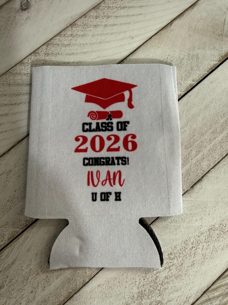 May include: White fabric can cooler with a red graduation cap and scroll design. Text includes "Class of 2026", "Congrats!", the name "Ivan", and "U of H". The can cooler has a black bottom.