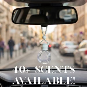 May include: A clear glass car air freshener bottle with a white ribbed cap and a white adjustable cord hanging from a rearview mirror. The text 10+ SCENTS AVAILABLE! is displayed in white capital letters across the bottom of the image.