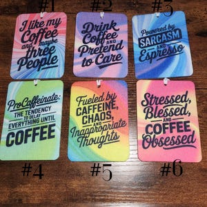 May include: Six rectangular air fresheners with rounded corners, each featuring a unique colorful swirl background and black text. The designs include phrases like I like my coffee and maybe three people, Drink Coffee and Pretend to Care, Powered by SARCASM AND Espresso, ProCaffeinate, Fueled by CAFFEINE, CHAOS, AND Inappropriate Thoughts, and Stressed, Blessed, AND COFFEE Obsessed.