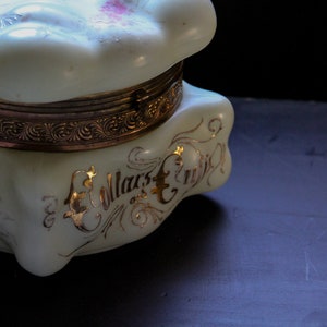 May include: A white porcelain trinket box with gold accents and floral designs. The box has a hinged lid and is decorated with the words "E. Mars & Co."