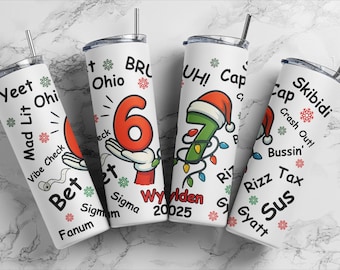 May include: Four white insulated tumblers with black text and festive graphics. Each tumbler features a different design, including the numbers 6 and 7, holiday decorations, and various slang terms. The tumblers have silver straws and black lids.