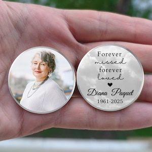 May include: Two round memorial keepsakes. One features a photo of a woman with gray hair, wearing a white sweater and necklace. The other has the text "Forever missed, forever loved" with a heart, the name "Diana Paquet" and the years 1961-2025.