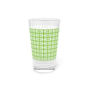 Puede incluir: Un vaso transparente con un patrón de cuadrícula verde en el centro. El patrón es una serie de cuadrados irregulares. El vaso está vacío y sobre un fondo blanco. El vaso es de tamaño estándar.
