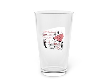 Può includere: Un bicchiere da pinta trasparente con un'illustrazione di una scena di caffè. Il disegno comprende un ombrellone rosso, una persona a un tavolo e la Torre Eiffel. Il testo sul bicchiere recita "Open Year Round" e "CAFE".