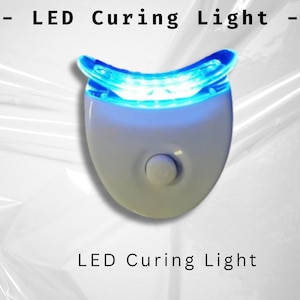 Könnte beinhalten: Weißes LED-Härtungslicht mit einem blauen Lichtring. Das Licht ist so konzipiert, dass es um die Zähne passt und einen Knopf an der Seite hat.