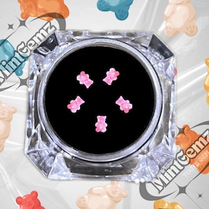May include: A clear glass jar with a black lid containing six pink gummy bear shaped nail charms. The jar is surrounded by gummy bear shaped charms in various colours.
