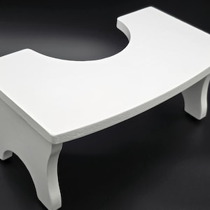 May include: A white wooden step stool with a curved top and a cutout section. The stool has a rectangular shape with curved edges and four legs. The step stool is painted white and appears to be made of wood.