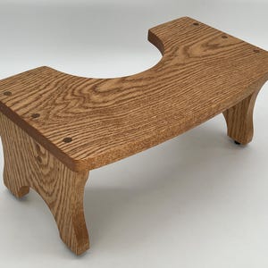 May include: A wooden toilet foot stool with a curved top and four legs. The stool is made of light brown wood with a natural finish.