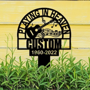 Pode incluir: Estaca de jardim de metal preto com o texto "Playing in Heaven" em um semicírculo acima de um violão e notas musicais. O texto "CUSTOM" está abaixo do violão e as datas "1960-2022" estão abaixo.