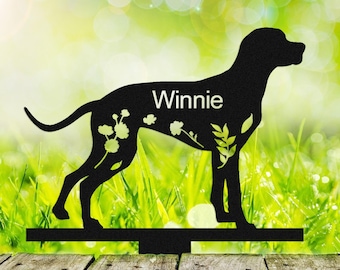 May include: Black metal silhouette of a dog with the name "Winnie" on the side. The silhouette is standing on a metal stake, which is mounted on a wooden surface.