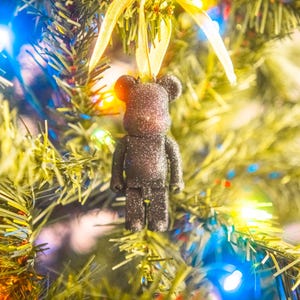 May include: A black glitter bear ornament hanging on a Christmas tree with yellow ribbon and colorful lights.
