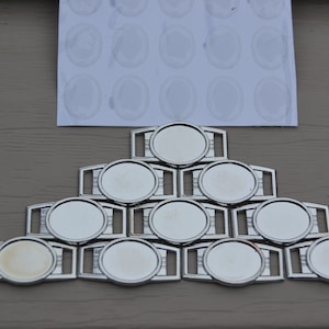 May include: A set of 10 silver-toned metal shoe charms with round, blank, clear, glass-like inserts. The charms are arranged in a pyramid shape.