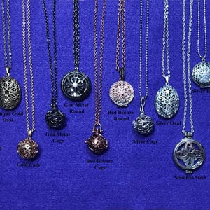 May include: A variety of silver, gold, and gunmetal charm necklaces with different cage and pendant styles. The pendants include round, oval, and tear shapes. The necklaces are displayed on a purple background.