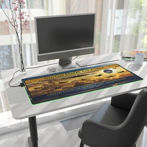 Peut inclure: Tapis de bureau rectangulaire avec un motif de coucher de soleil, des silhouettes d'avions et le texte "UNITED STATES AIR FORCE". Le tapis commémore le 250e anniversaire des États-Unis d'Amérique. Il a une bordure verte éclairée.