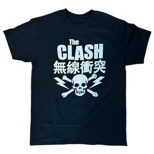 May include: Black t-shirt with a white graphic of a skull and crossbones with lightning bolts. The text "The Clash" and "無縁 衝突" are printed on the shirt.