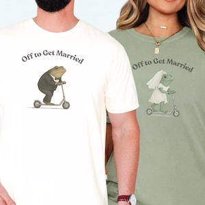 May include: Ivory and bay-colored t-shirts with the text "Off to Get Married" above a frog illustration. The frog on the ivory shirt wears a suit and rides a scooter. The frog on the bay shirt wears a wedding dress and veil and rides a scooter.