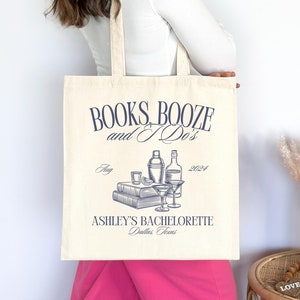 May include: Cream-colored tote bag with navy blue text and illustrations. The bag reads "BOOKS, BOOZE and I Do's" with a graphic of books, cocktail glasses, and bottles. Below the graphic is "ASHLEY'S BACHELORETTE Dallas, Texas".