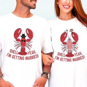 May include: White t-shirts with a red lobster graphic. The lobster on the left wears a black hat and bow tie, while the lobster on the right has flowers. Text reads "SHELL YEAH, I'M GETTING MARRIED!"