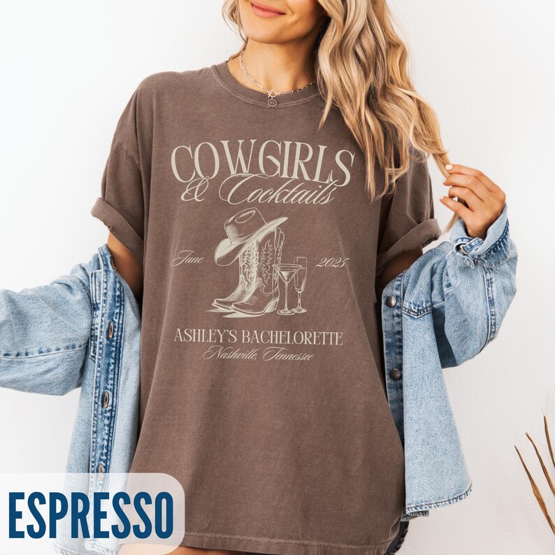 May include: Espresso-colored t-shirt with the text "Cowgirls & Cocktails" and a graphic of a cowboy hat, boots, and champagne flutes. The shirt also includes the text "Ashley's Bachelorette Nashville, Tennessee" and the date "June 2025".