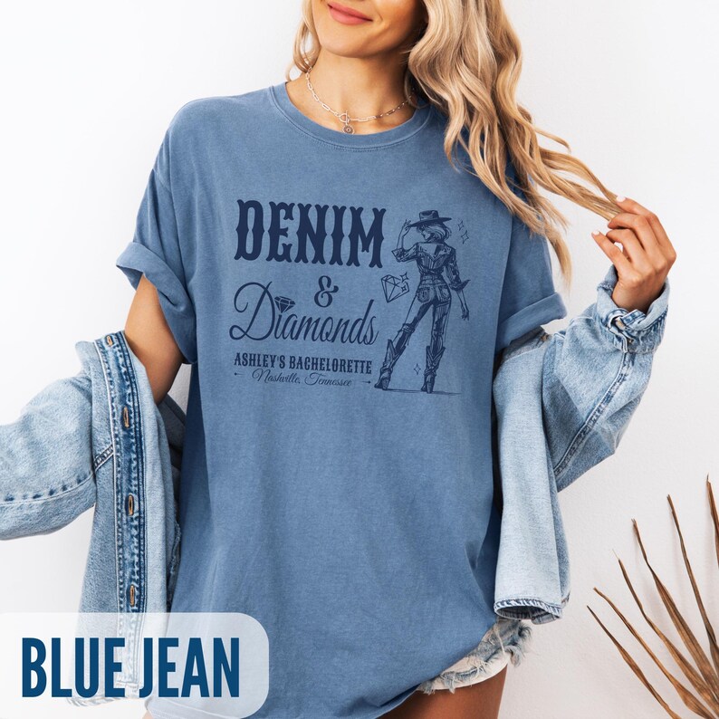 Puede incluir: Una camiseta azul vaquero con el texto "Denim & Diamonds" y un gr&aacute;fico de una mujer con un sombrero de vaquero y botas. El texto debajo del gr&aacute;fico dice "Ashley's Bachelorette - Nashville, Tennessee".
