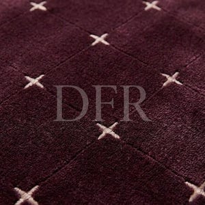 May include: A deep plum-coloured textile featuring a grid pattern formed by recessed lines. Small, light-coloured embroidered cross-stitch details are positioned at each intersection of the grid. The letters DFR are centred in the image.