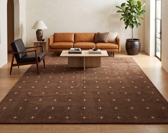 May include: A large rectangular area rug in a deep brown hue, featuring a repeating pattern of small, light-coloured cross-shaped symbols evenly spaced across the entire surface, providing a textured foundation for the living room space.