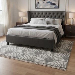 May include: A grey upholstered bed with a buttoned headboard and a patterned rug. The bed is made up with white bedding and a grey throw. Two matching bedside tables with lamps are on either side of the bed.