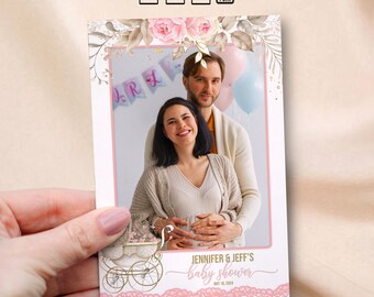May include: A pink and white photo booth prop with a floral design and a white baby carriage. The text "Jennifer & Jeff's baby shower" is written in gold script with the date "May 18, 2024" below.