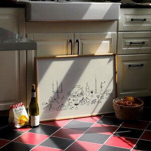 Op de afbeelding: Een ingelijste illustratie van een feestelijk diner, met een kalkoen, kaarsen en wijnglazen. Een fles wijn en een zak pasta staan naast de lijst. Een mand met sinaasappels staat op een rood-zwarte geblokte vloer.