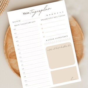 May include: A printable daily planner in white with a beige background. The planner has a section for the date, a section for daily tasks, a section for priorities, and a section for tracking water intake. The planner also has a section for writing down things you are grateful for.
