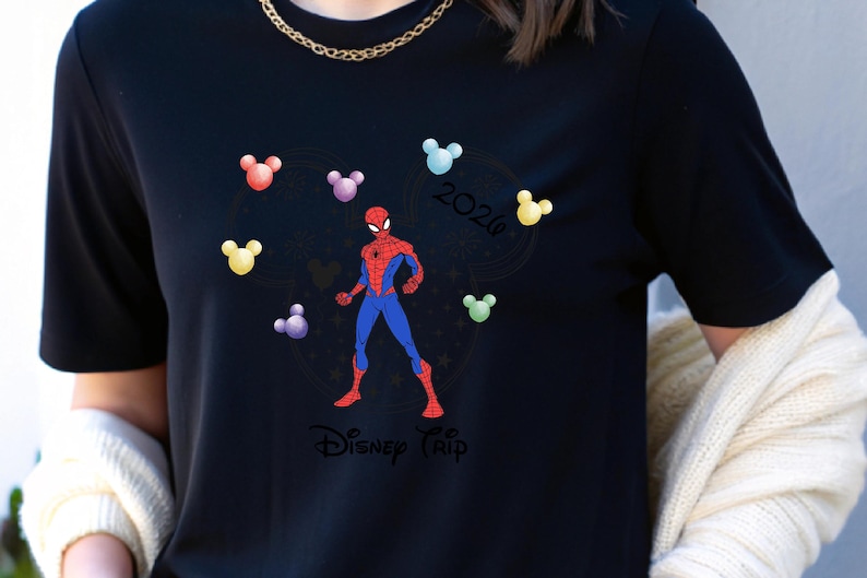 May include: Black t-shirt with a Spider-Man design in red and blue, encircled by colourful Mickey Mouse head shapes. The shirt also features the text "Disney Trip 2020" in a circular design.