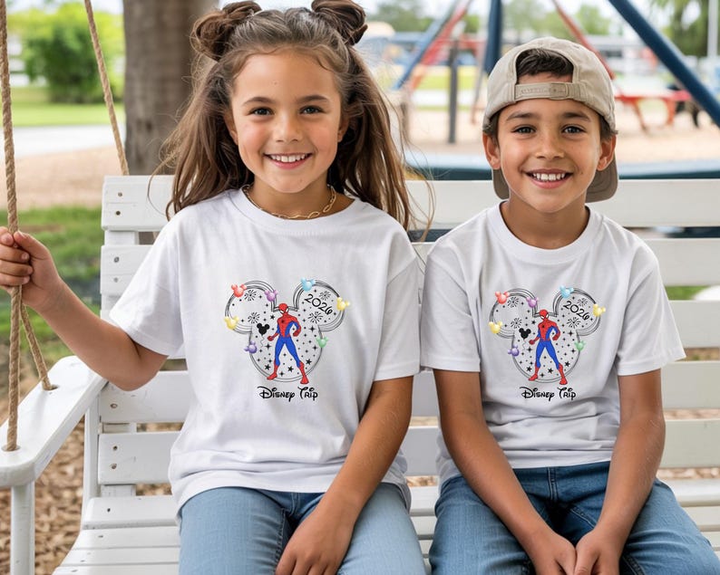 May include: Two children wearing white t-shirts with a Disney-themed graphic. The graphic features a Mickey Mouse head outline with a Spider-Man figure, the year 2024, and the words "Disney Trip". The children are smiling.