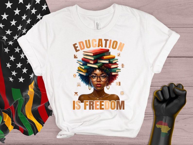 May include: White t-shirt with the words "EDUCATION IS FREEDOM" and an illustration of a person with books on their head. The illustration features a person with glasses and curly hair. A black power fist and a flag with stars and the colors red, black, and green are also visible.