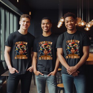 May include: Three people wearing black t-shirts with the words "EDUCATION IS FREEDOM" printed on them. The graphic features a person with glasses and a stack of books on their head. The design is in shades of brown, red, and blue.