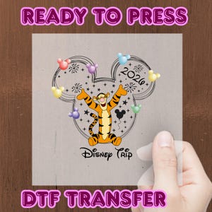 Könnte beinhalten: Ein DTF-Transfer mit Tigger aus Winnie Puuh, einer Mickey Mouse-Kopfkontur, Feuerwerk und dem Text "Disney Trip 2026". Die Wörter "READY TO PRESS" und "DTF TRANSFER" sind ebenfalls abgebildet.