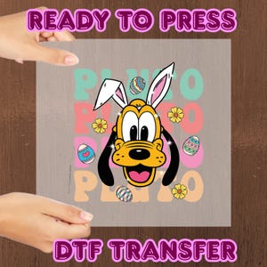 Pode incluir: Uma transferência DTF cinza com Pluto usando orelhas de coelho, com o texto "READY TO PRESS" e "DTF TRANSFER" em rosa. O design inclui a palavra "PLUTO" em cores pastel, ovos de Páscoa e flores amarelas.