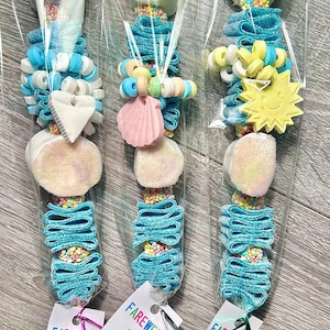 May include: Three candy skewers in clear plastic packaging. Each skewer features a large marshmallow, blue candy ribbons, and various candies, including a heart, a seashell, and a smiling sun. Each skewer has a tag that says "Farewell 4th Grade!"