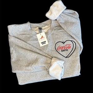 May include: Gray sweatshirt with a red and black Coca-Cola Zero heart design embroidered on the front.