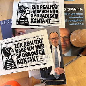 Könnte beinhalten: Zwei weiße rechteckige Papierdrucke mit einer schwarzen Linolschnitt-Illustration einer Person im Profil und dem Text ZUR REALITÄT HABE ICH NUR SPORADISCH KONTAKT, platziert auf Büchern und Holzbildhauerwerkzeugen auf einer hellen Holzoberfläche.