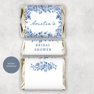 Könnte beinhalten: Drei Mini-Schokoriegel, verpackt in Goldfolie. Der obere Riegel trägt den Namen "Amelia's" in Schreibschrift, umgeben von blauen Blumendesigns. Der mittlere Riegel trägt die Aufschrift "BRIDAL SHOWER" in blauer Schrift. Der untere Riegel zeigt blaue Blumendesigns.