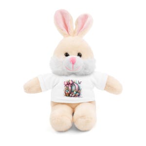 Op de afbeelding: Een witte pluche konijn met een wit T-shirt met een kleurrijk paasei-ontwerp. Het konijn heeft roze oren en een wit gezicht.
