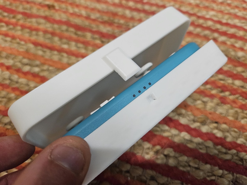 May include: A white rectangular case with a blue rectangular object inside. The case has a hinged lid and a small latch. The blue object has four small, evenly spaced dots.