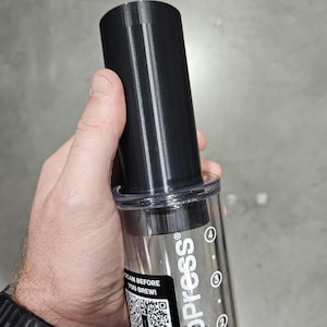 以下が含まれることがあります： 透明なチャンバーと黒いフィルターが付いた黒いAeroPressコーヒーメーカー。チャンバーには1、2、3、4オンスの目盛りが付いています。AeroPressのロゴはチャンバーの側面に印刷されています。